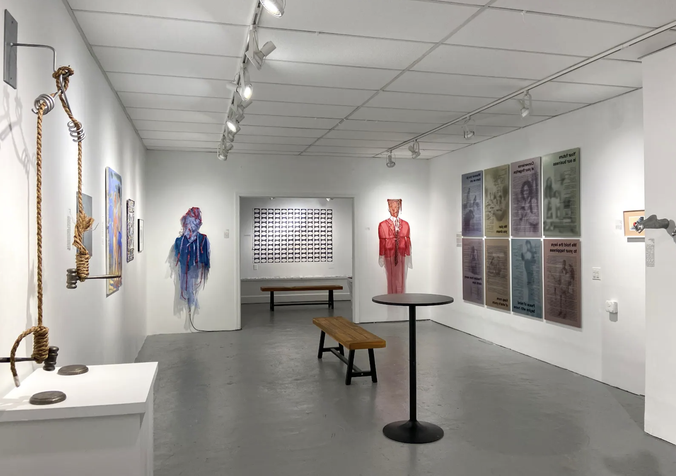 Gallery space containing two costumed figures, prints, and a sculpture made with rope